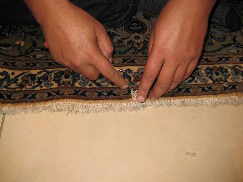 Réparation Tapis Persan - Laine Artisan remplissant de la laine dans un tapis persan endommagé par les mites