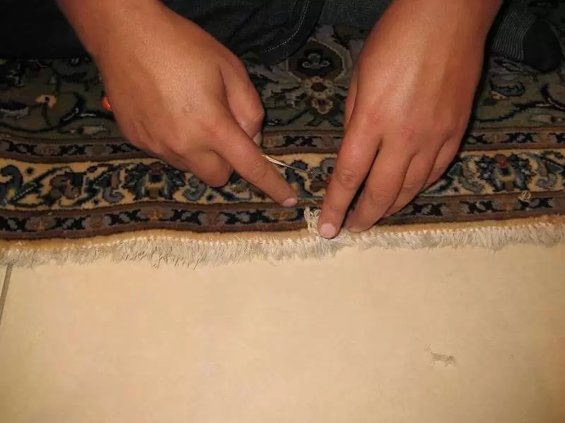 Artisan remplissant de la laine dans un tapis persan endommagé par les mites