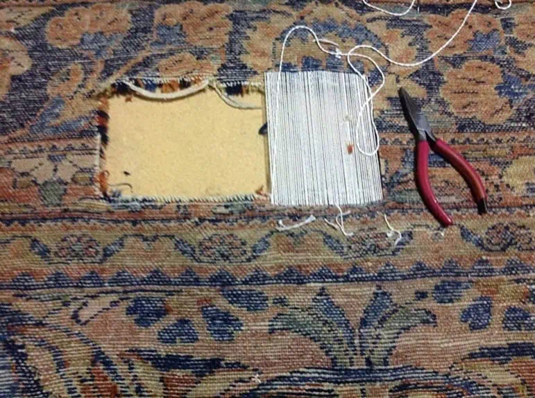 Réparation en cours d'un grand trou sur un tapis persan