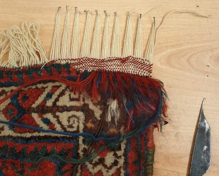 Restauration de franges neuves et réparation d'un trou sur un tapis, travail en cours